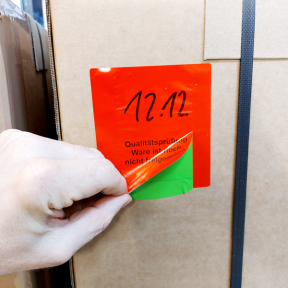 QS-Label-Wareneingang 2x klebt auf Verpackung und Oberetikett wird abgezogen, darunter ist der grüne Abschnitt zu sehen 